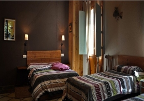 Dormitorio triple con pared oscura y colchas de detalles geométricos en la casa rural