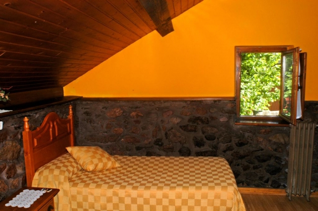 Dormitorio con techo abuhardillado y pared con piedras