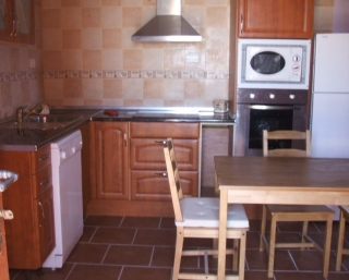 Cocina en madera con mesa delante y muchas sillas