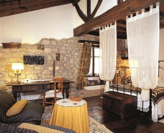 Habitación con cama de matrimonio, paredes de piedra y techos abuhardillados