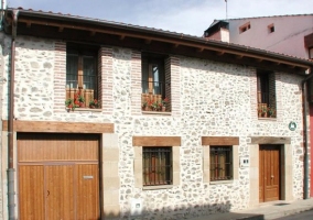 Fachada principal de la vivienda, en piedra y con flores en las ventanas superiores